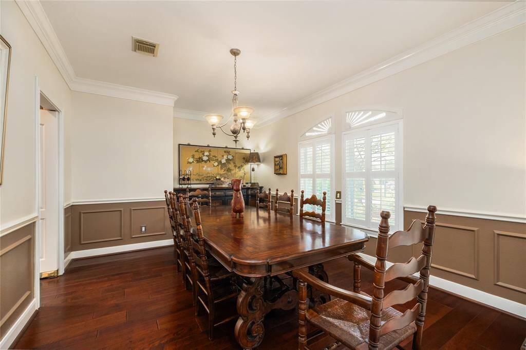 Where every gathering feels special. This refined dining room offers timeless charm with rich wood flooring, graceful arched windows adorned with plantation shutters, and elegant wainscoting. A sophisticated chandelier casts a warm glow over the space—perfect for intimate dinners or celebratory moments shared around the table.