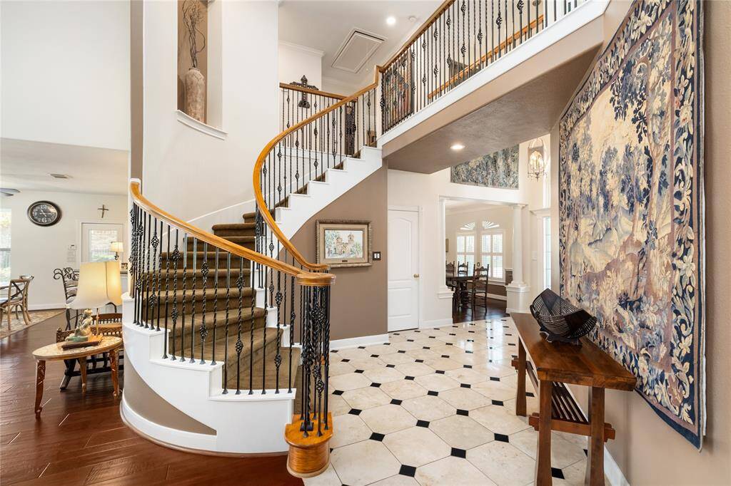 A grand welcome home. This stunning foyer makes a lasting impression with its sweeping curved staircase, intricate wrought iron railings, and soaring ceiling. The seamless blend of tile and wood flooring guides you effortlessly into the heart of the home. Bright, open, and undeniably inviting.