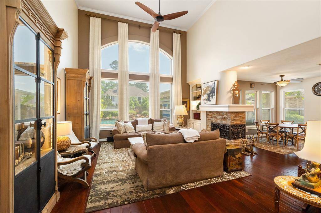 Comfort meets sophistication. This beautifully appointed living space showcases tall windows that frame backyard views and bathe the room in natural light. A cozy fireplace anchors the room, flanked by elegant built-ins and enriched by warm wood tones—creating a harmonious blend of refined style and everyday comfort.