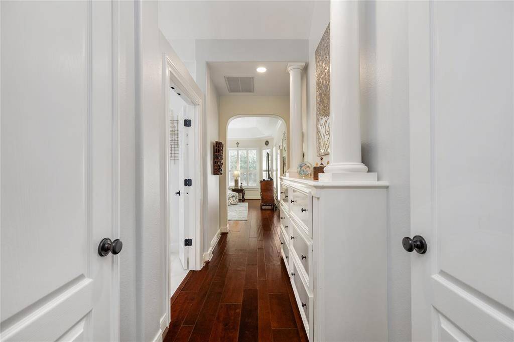 A graceful transition through the heart of the home. This light-filled hallway features gleaming wood floors, crisp white walls, and elegant architectural details like decorative columns and built-in cabinetry. As it opens into a sun-drenched living area framed by expansive windows, the space feels both refined and effortlessly welcoming.