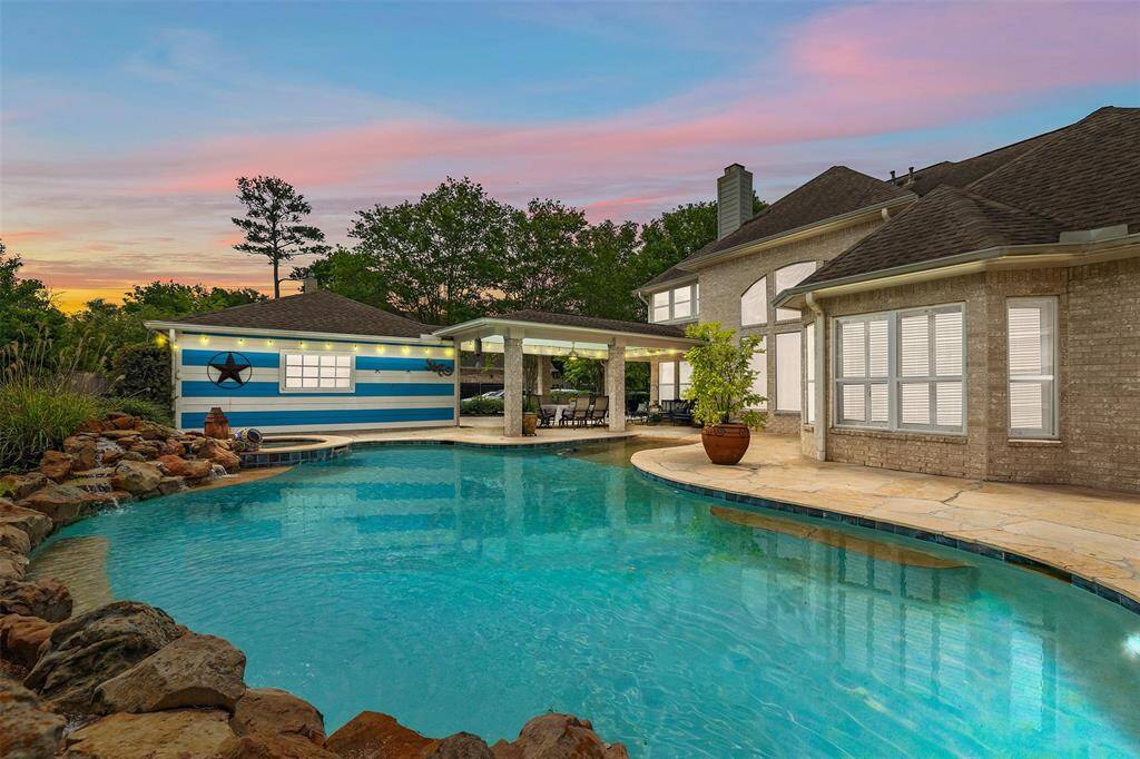 Your private retreat awaits. This resort-style backyard features a sparkling pool framed by a stone patio and lush landscaping—designed for both relaxation and unforgettable gatherings. With a covered seating area and the glow of a sunset sky overhead, every evening here feels like a getaway.