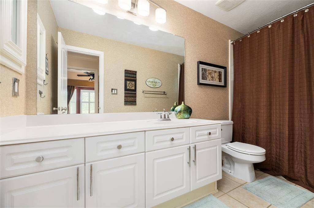 This spacious bathroom boasts a large white vanity with generous storage, complemented by a full-length mirror and contemporary lighting. The neutral tones of beige walls and the clean design of the shower create a serene, inviting atmosphere that feels both fresh and timeless.