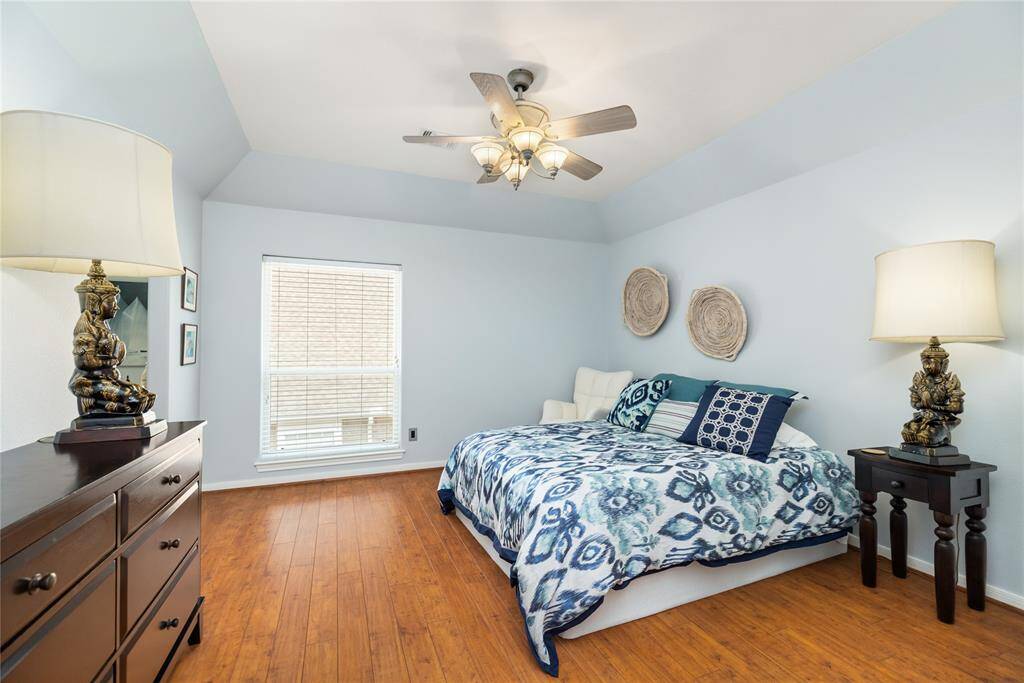 This secondary bedroom offers soft blue tones, warm wood flooring, and a spacious layout that invites rest and relaxation. A large window allows sunlight to pour in, while the ceiling fan adds year-round comfort—making it an ideal retreat for family or guests.