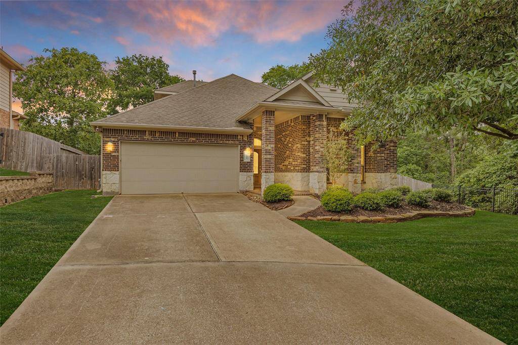 This photo showcases a charming home with a brick exterior, a well-maintained lawn, and a spacious driveway leading to a two-car garage. The house is surrounded by lush greenery, offering a serene and inviting atmosphere.