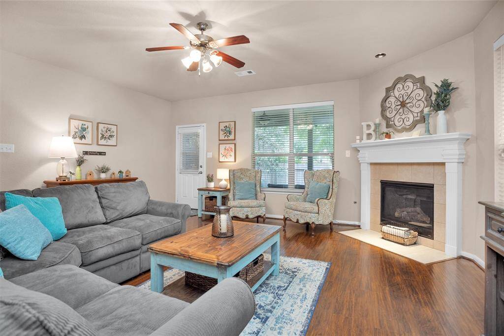 This cozy living room features a warm fireplace.  The space is complemented by hardwood floors, a ceiling fan with lights,  creating a welcoming and comfortable atmosphere.