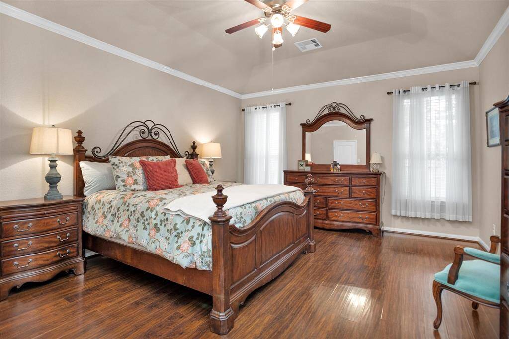 Large primary bedroom with elegant hardwood floors, abundant natural light, and classic furnishings for a cozy retreat.