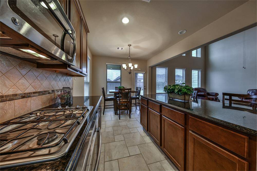 Gourmet kitchen showcases upgraded stainless steel built-in appliances and a stylish tile backsplash with custom mosaic inserts laid in a designer pattern. Open to the casual dining area, surrounded by windows that flood the space with natural light.
