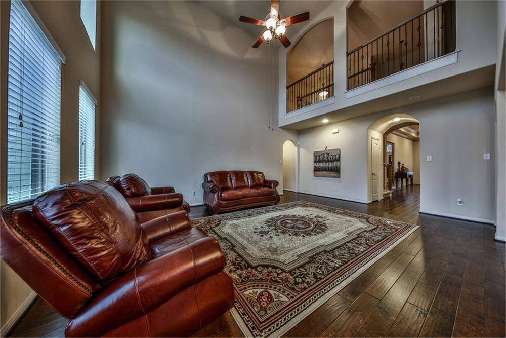 Grand living area boasts soaring two-story ceilings, rich upgraded wood floors, and a striking iron catwalk that adds architectural elegance and charm.