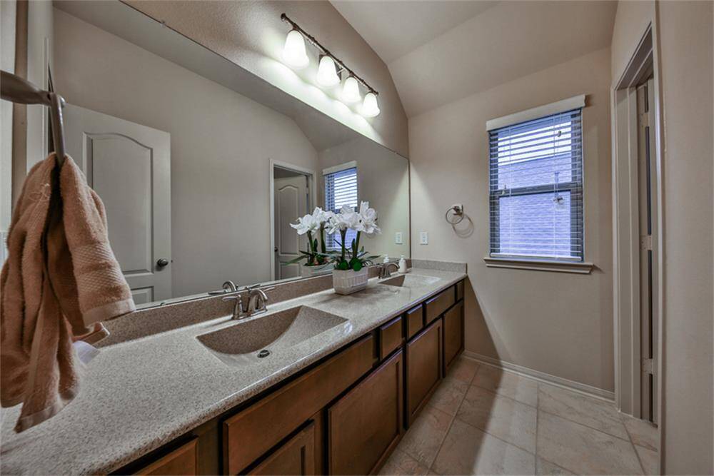 The children’s bathroom features upgraded solid surface countertops with dual sinks, stylish cabinetry, and upgraded light fixtures. Large tile flooring laid in a designer pattern adds elegance, and the enclosed tub/shower combo offers both function and comfort.