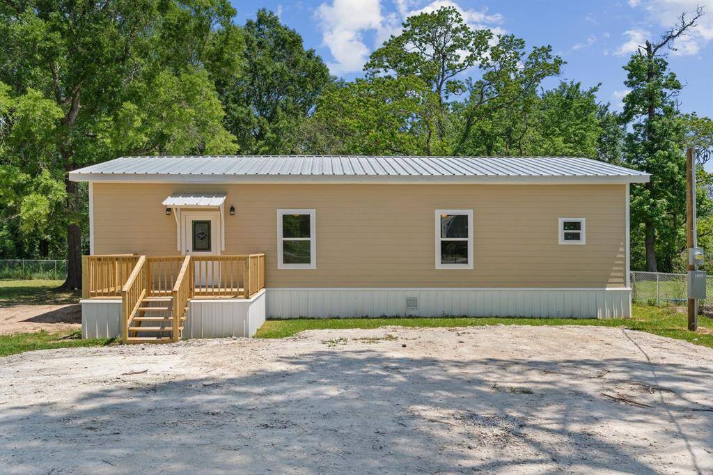 This charming home features a simple, modern facade with a metal roof and light-colored siding. It has a welcoming front porch with steps and a spacious yard, surrounded by lush trees for added privacy. Ideal for those seeking a serene living environment.