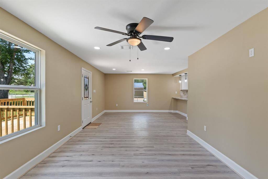Bright and open living space with neutral walls and light wood flooring, featuring a ceiling fan. The room offers plenty of natural light from large windows and has easy access to an outdoor deck, perfect for entertaining.