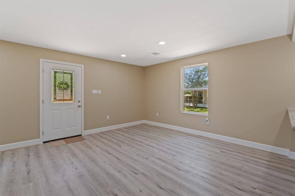 Bright, open room with light wood flooring and neutral walls. Features a decorative front door and a window providing natural light. Ideal for a cozy living space.