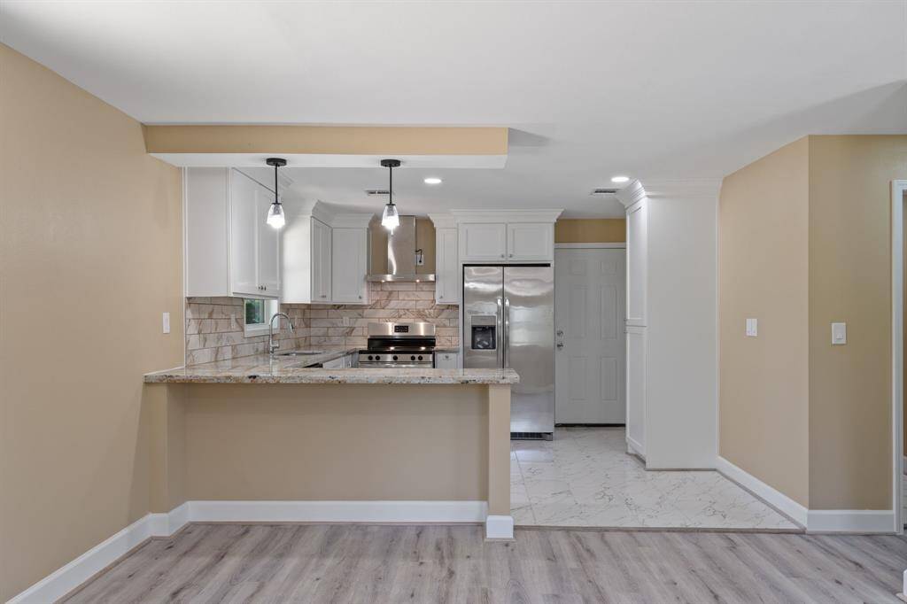 This photo showcases a modern kitchen with granite countertops, stainless steel appliances, and stylish pendant lighting. The open layout features light wood flooring and a tiled cooking area, providing a fresh and inviting space.