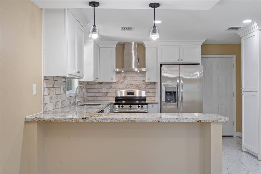Modern kitchen with stainless steel appliances, white cabinetry, and a granite countertop. Features a tiled backsplash, pendant lighting, and a breakfast bar. Bright and inviting space.