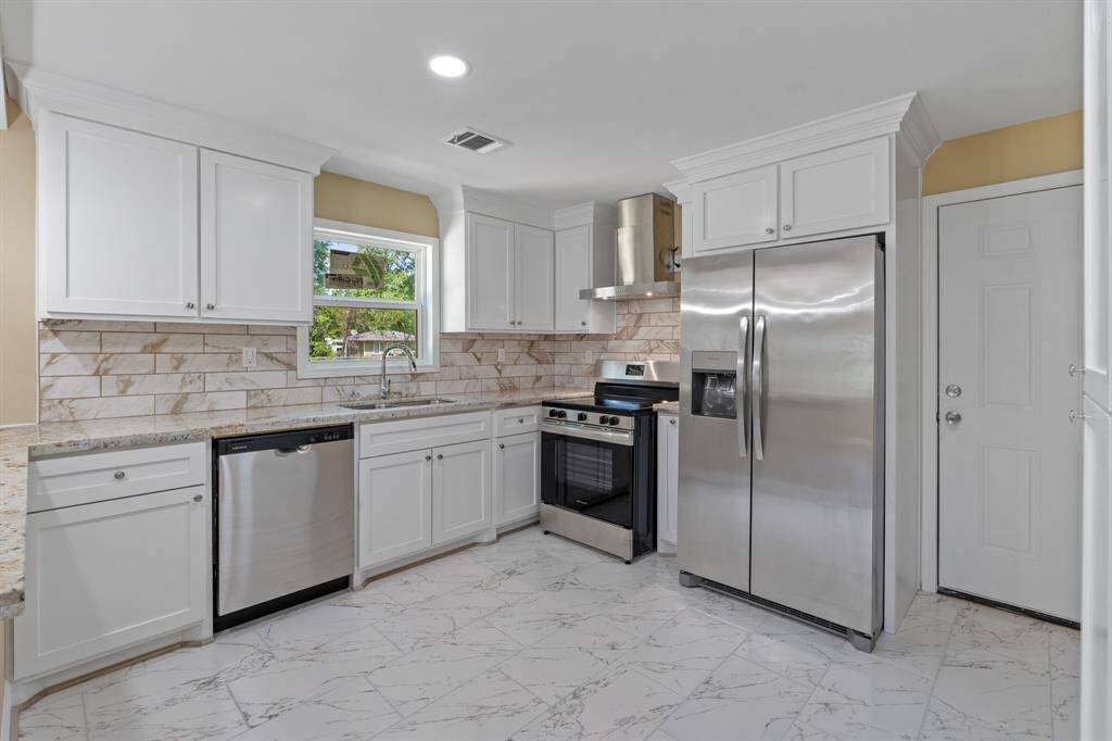Modern kitchen with stainless steel appliances, white cabinetry, and granite countertops. Features a tile backsplash and floor, offering a bright and clean look.