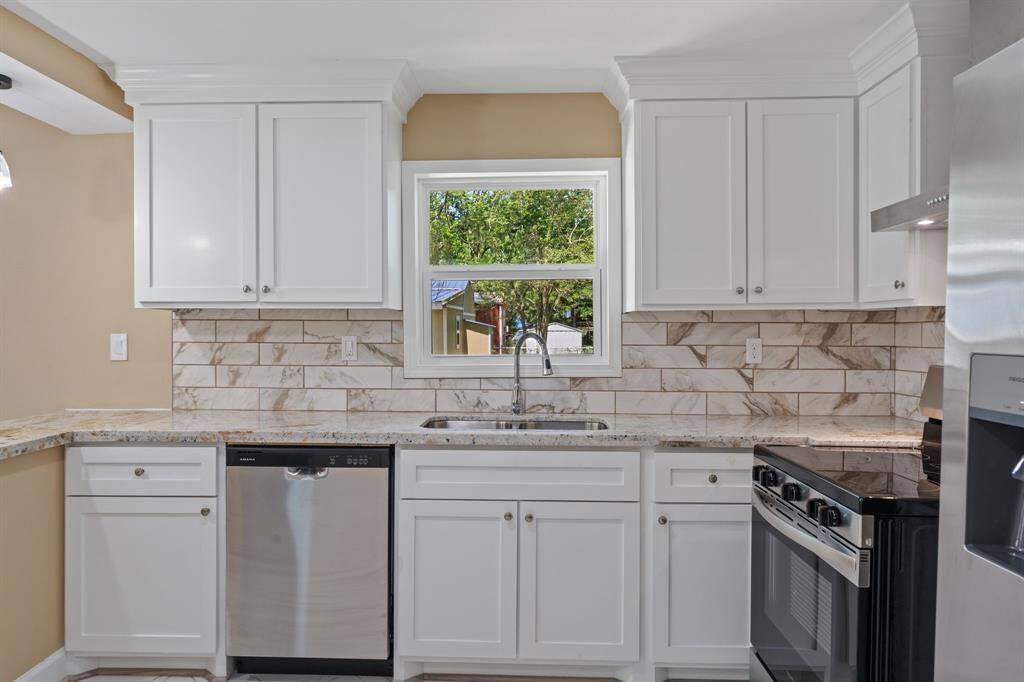 This kitchen features a modern design with white cabinetry, a stylish marbled tile backsplash, and stainless steel appliances, including a dishwasher and a stove. The window above the sink allows natural light to brighten the space.