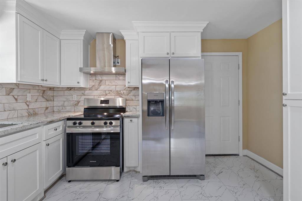 Modern kitchen with stainless steel appliances, including a refrigerator and stove. The space features white cabinetry, marble-patterned tile backsplash, and a matching tile floor, creating a clean and contemporary look.
