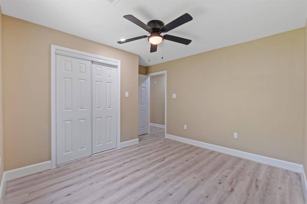 This room features light wood flooring, neutral beige walls, a ceiling fan, and a double-door closet, offering a clean and modern look.
