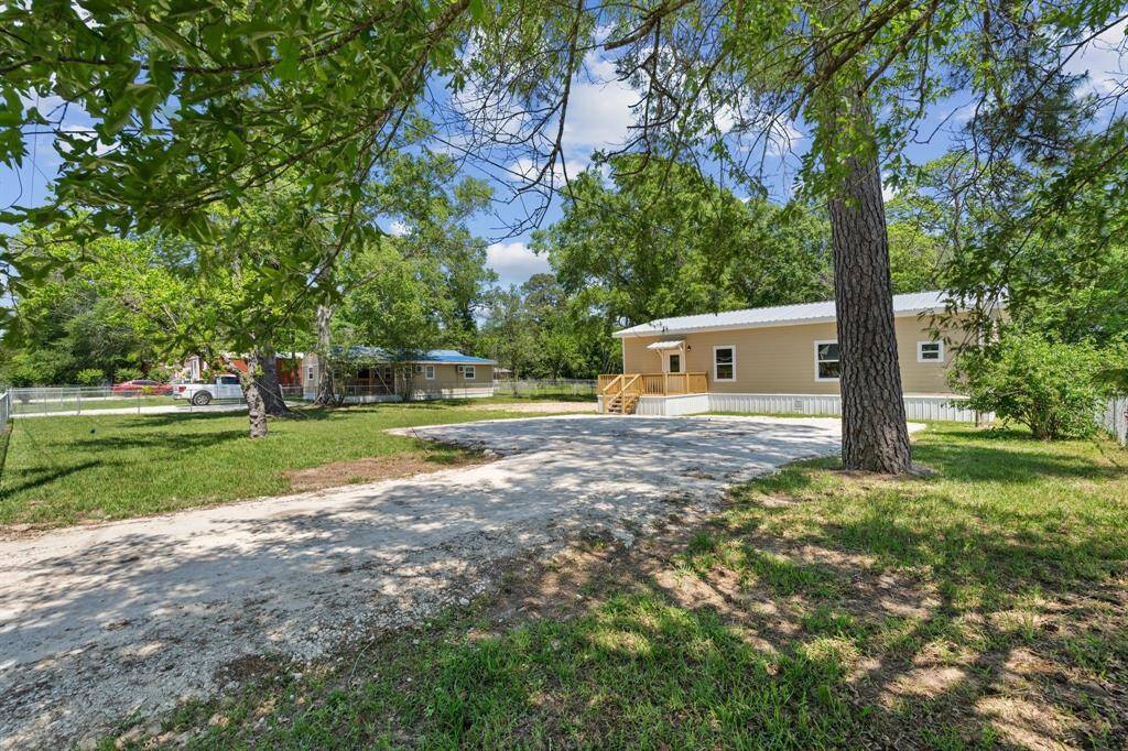 This property features a charming, single-story home with a light exterior, nestled among mature trees. It boasts a spacious front yard with a gated driveway and a small porch, offering a serene, natural setting.