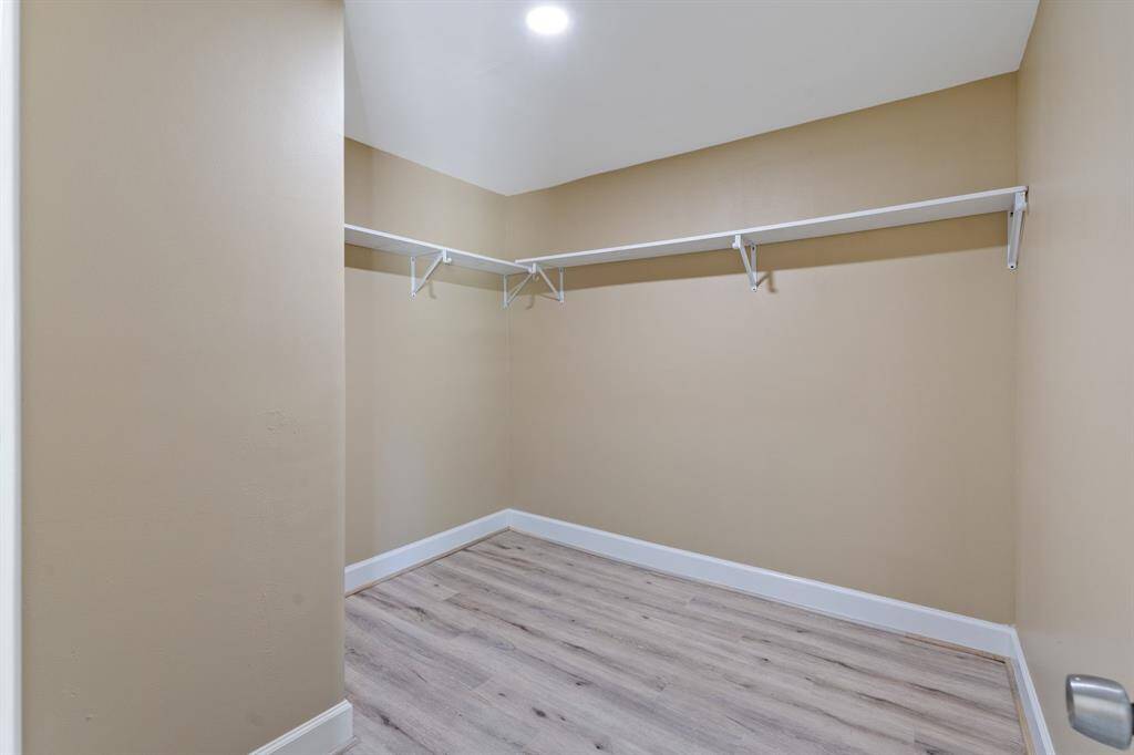 Spacious primary walk-in closet with light wood flooring, neutral walls, and ample shelving for storage.