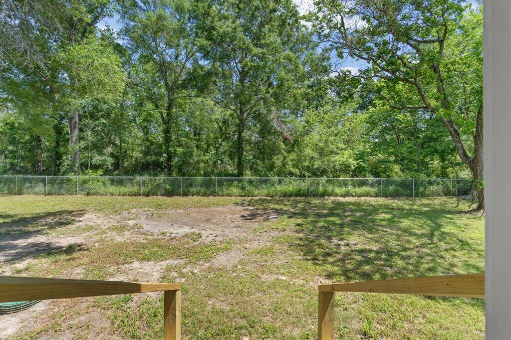 This photo features a spacious backyard with partial grass and dirt areas, bordered by a fence. It's surrounded by lush, mature trees, providing a natural and private setting.