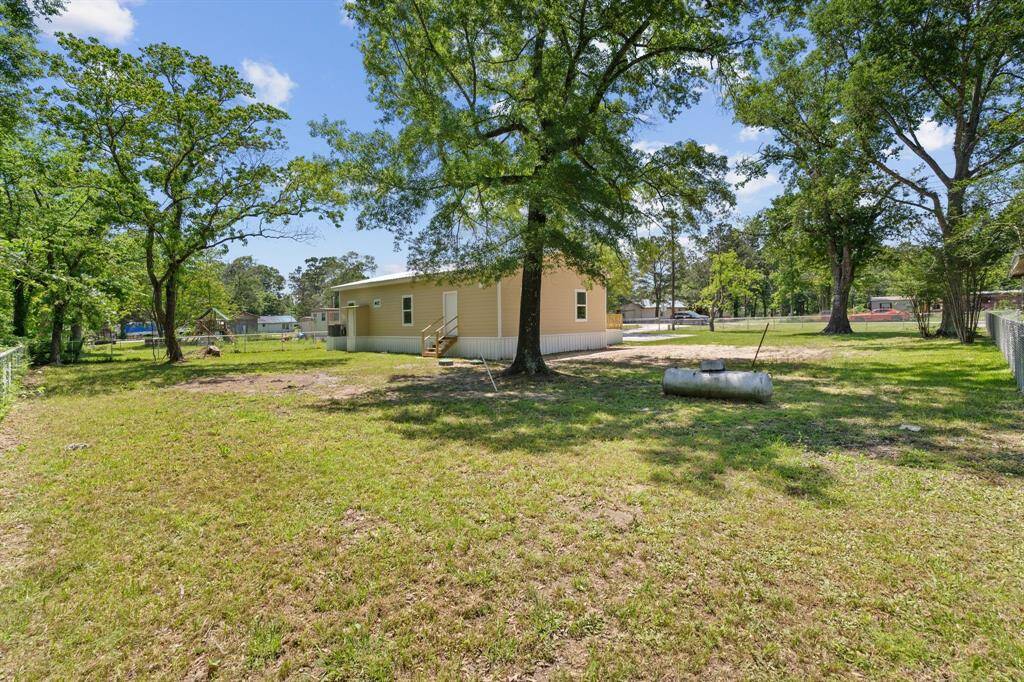 This photo showcases a spacious backyard with mature trees, offering ample shade and privacy. The area features a well-maintained lawn, bordered by a fence, and includes a light-colored house with a small deck. Ideal for outdoor activities and relaxation.
