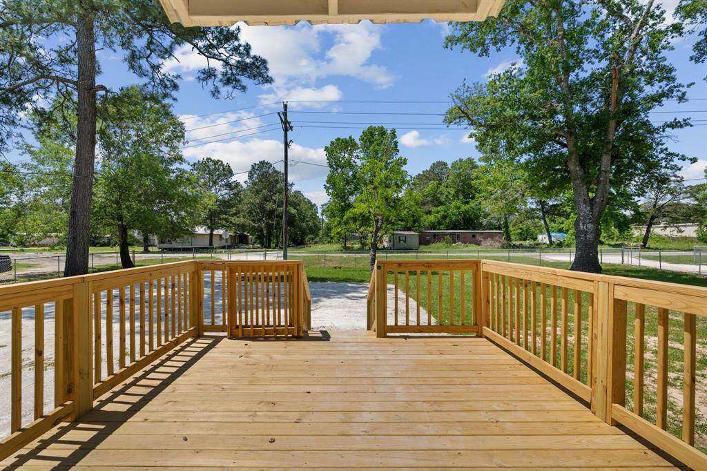 This photo showcases a spacious wooden deck attached to a home, offering a view of a grassy yard and mature trees. The area is open and bright, making it ideal for outdoor relaxation or entertaining.