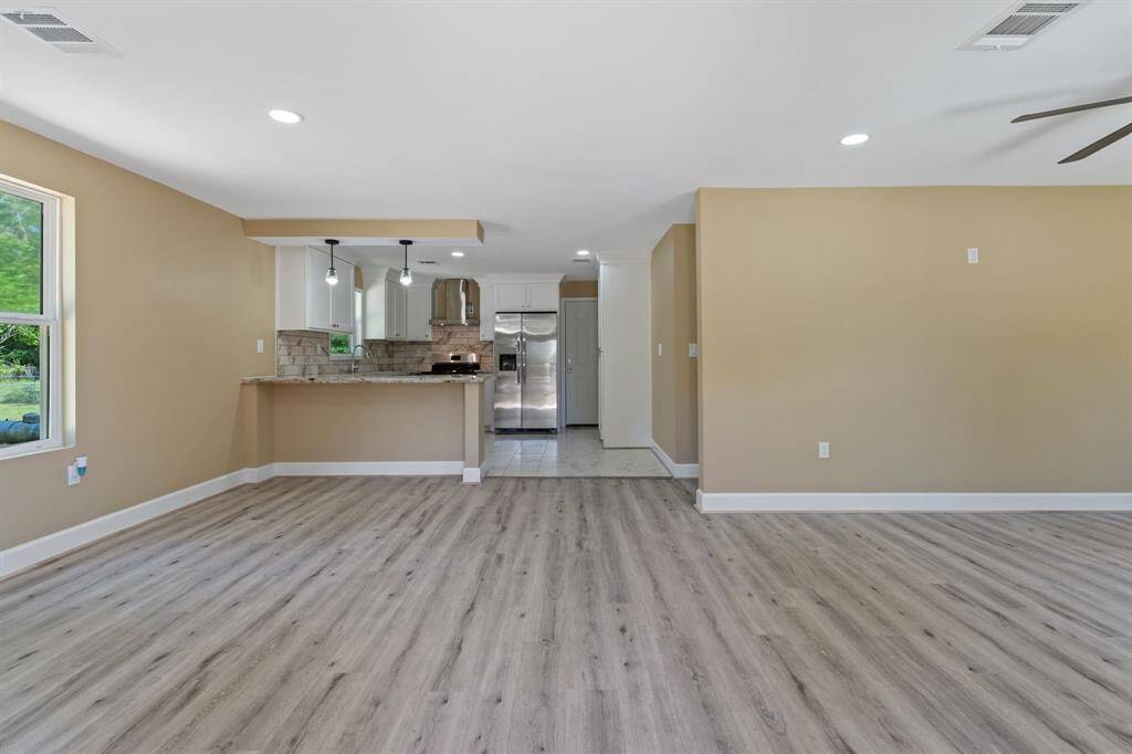 This modern open-concept space features light wood flooring, neutral walls, and recessed lighting. The kitchen, with a breakfast bar, has stainless steel appliances and stylish pendant lights, creating a bright and inviting area perfect for entertaining.
