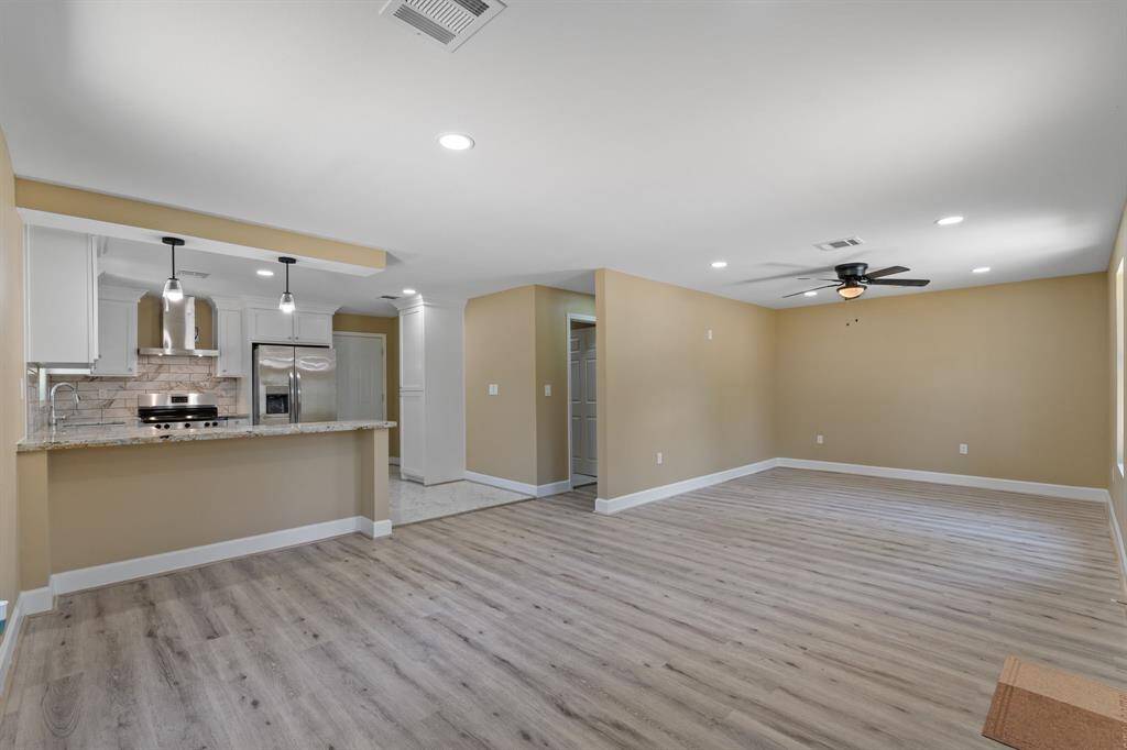 This spacious open-concept living area features modern laminate flooring, neutral walls, and recessed lighting. The kitchen is equipped with stainless steel appliances, a tiled backsplash, and an island with pendant lighting, perfect for entertaining.