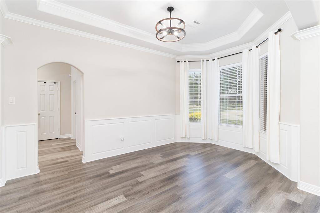 Bright, inviting dining room with large windows and elegant crown molding. Features modern flooring, wainscoting, and a stylish light fixture. Perfect for a dining or sitting area.