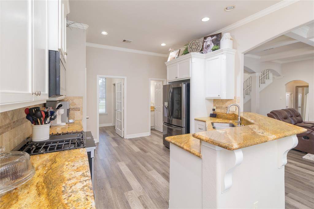 This kitchen features GAS cooktop, granite countertops, white cabinetry, and stainless steel appliances. It opens to a spacious living area with modern flooring and plenty of natural light.