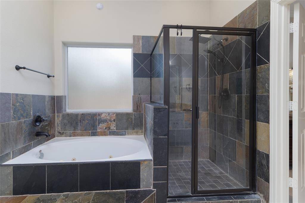 This bathroom features a modern design with a spacious soaking tub and a separate glass-enclosed shower. The slate tile adds a touch of elegance, complemented by a frosted window for privacy.