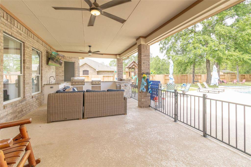 Spacious covered patio with ceiling fans, outdoor seating, and a built-in grill area. Overlooks a fenced-in pool with Pebble Tec, slide, water feature, and a fire pit, perfect for entertaining.