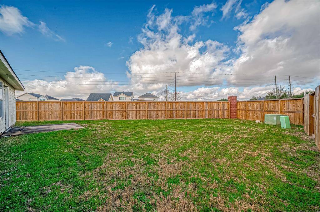 The backyard stretches across a wide, grassy expanse, enclosed by a wooden fence for privacy.