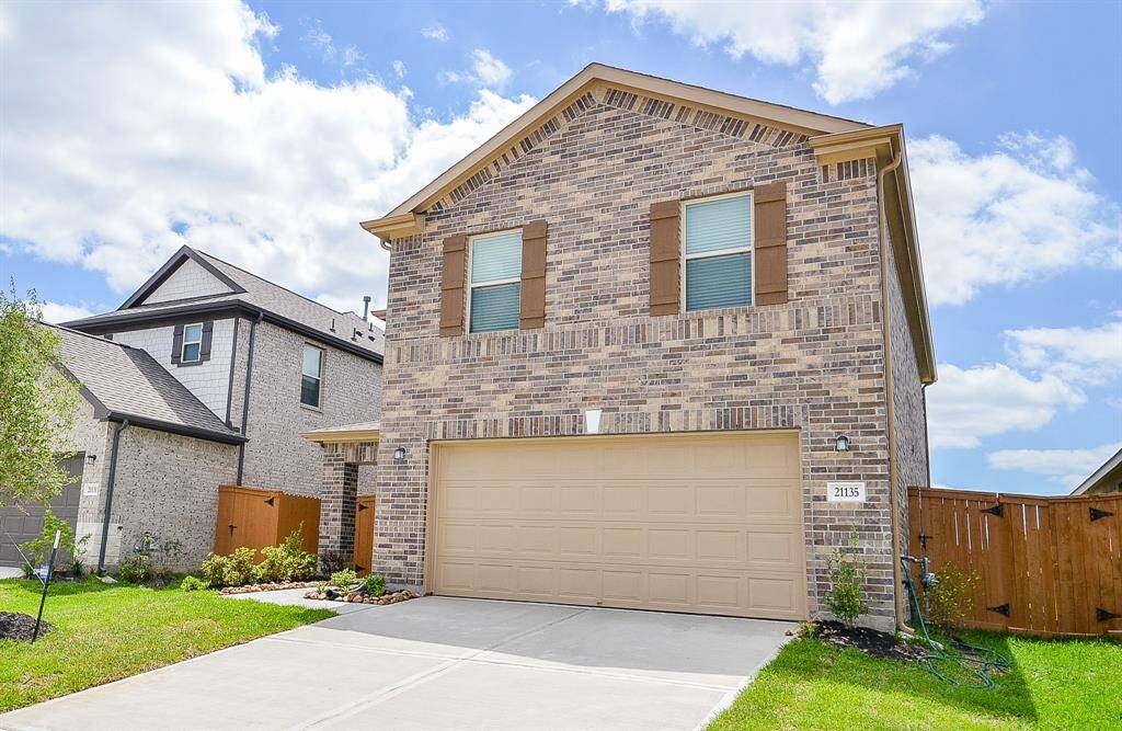 This is a modern two-story brick home with a gabled roof and a two-car garage. The property features neatly landscaped front yard and wooden shutters on the windows, adding a touch of warmth and character. Situated in a suburban neighborhood, it offers a spacious driveway and fenced backyard.