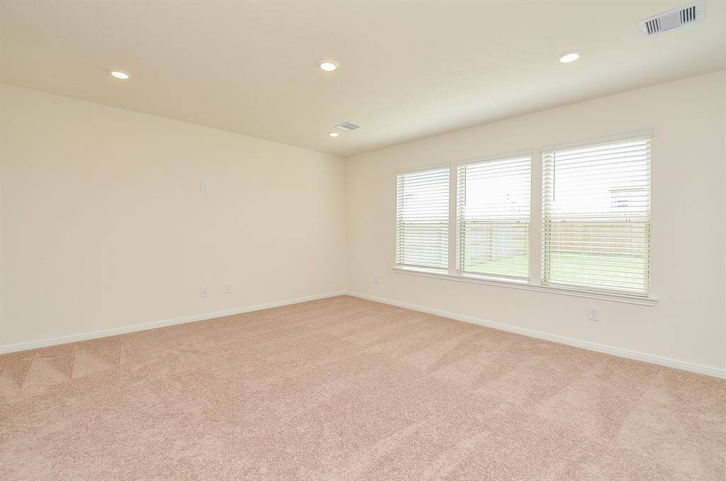 This Living room features neutral carpeting, recessed lighting, and large windows offering ample natural light and a view of the backyard.