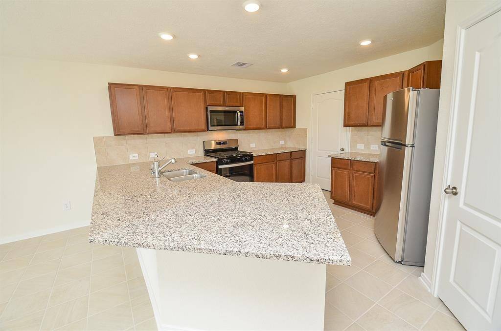 This modern kitchen features granite countertops, stainless steel appliances, ample wooden cabinetry, and recessed lighting, offering a spacious and functional cooking area.