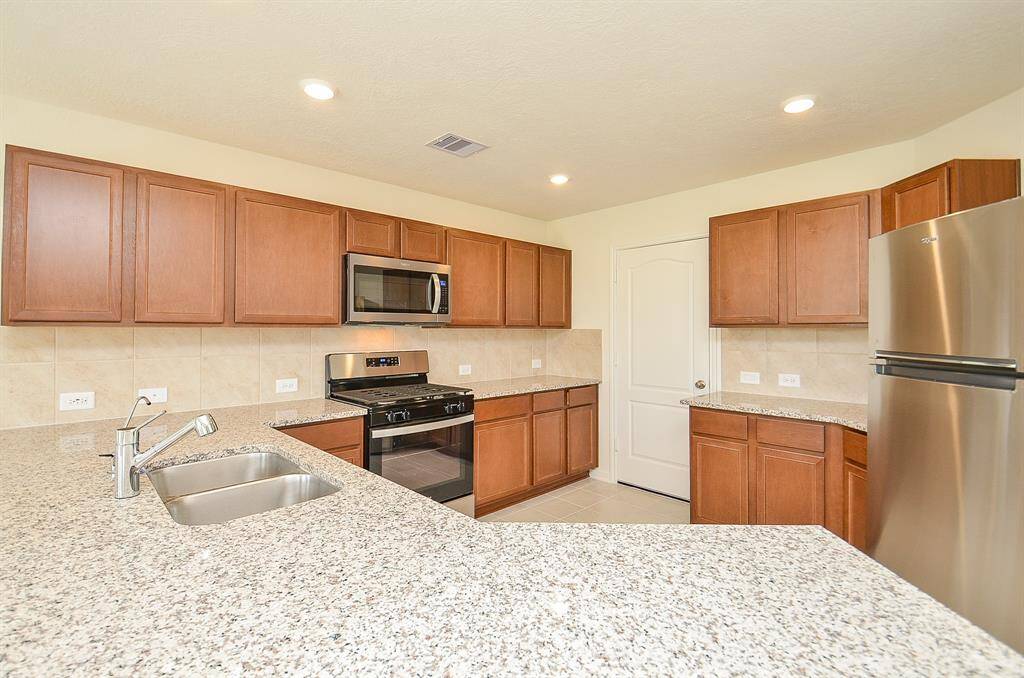 This kitchen features modern stainless steel appliances, granite countertops, and ample wooden cabinetry. The light tile flooring complements the neutral walls, creating a bright and inviting space.