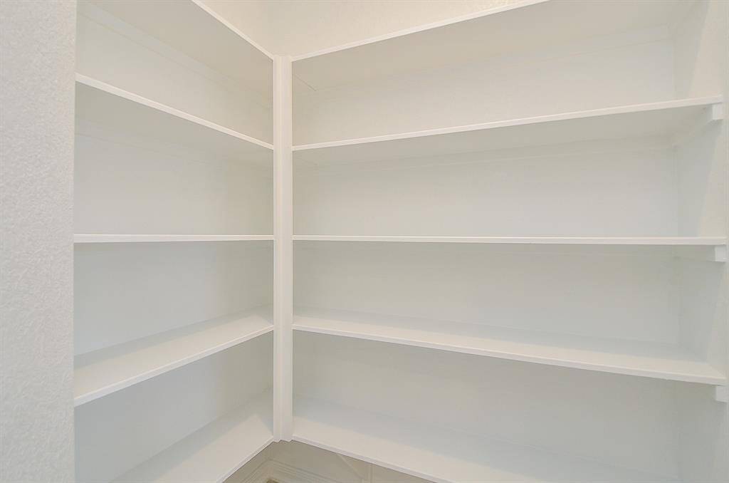 This photo shows a spacious, well-lit pantry with built-in white shelving, providing ample storage for kitchen essentials.