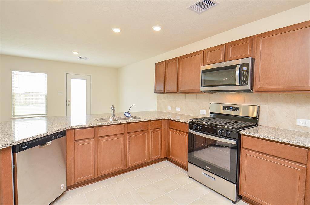 Modern kitchen with stainless steel appliances, granite countertops, and ample cabinetry. Well-lit with a view of the backyard through a glass door.