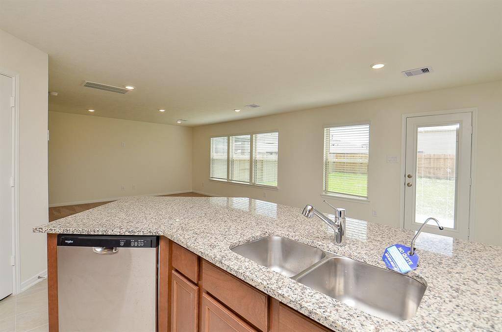 This view of the Kitchen/Living room features neutral walls and carpet, ample natural light through two windows with blinds, and a simple, clean design perfect for personalization.