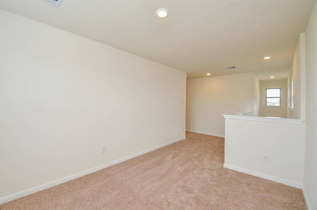 This photo shows the Game room and a bright, open hallway area with neutral-colored walls and carpet. It features recessed lighting and a short railing, leading to a window at the end, creating an inviting, airy space.