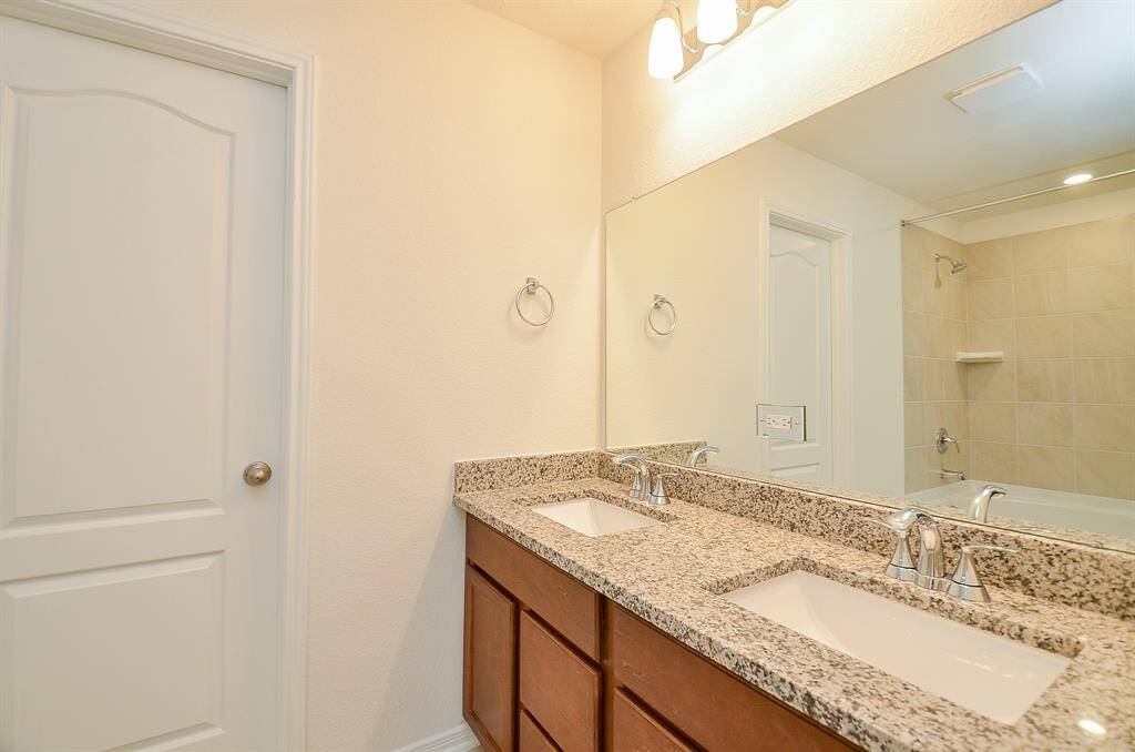 The Primary Bath with Double Sinks and Granite Countertop featuring Large Mirror and Light Fixtures.