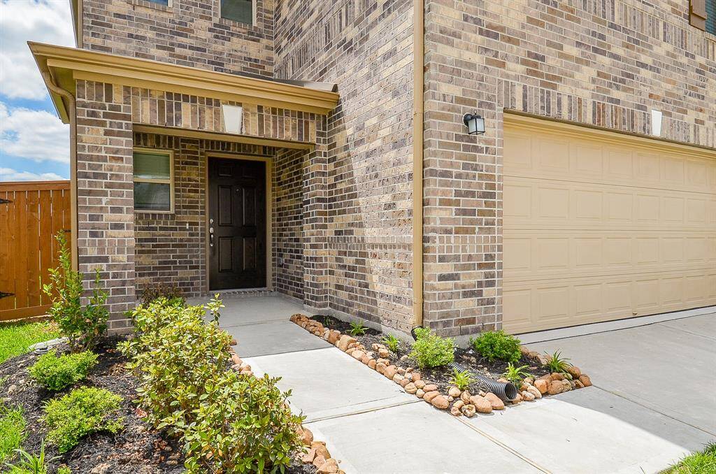 This photo shows a modern brick home with a welcoming front entrance and two-car garage. The well-maintained landscaping features shrubs and a pathway leading to the front door.
