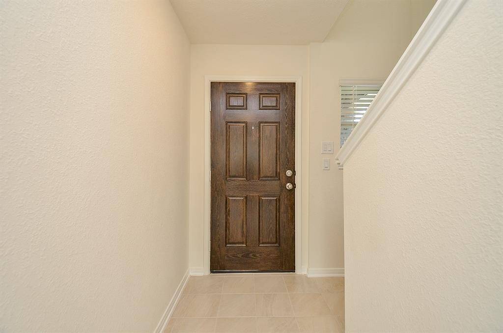 This photo shows a clean and bright entryway with a wooden front door and light-colored tile flooring. The walls are neutral, creating a welcoming and spacious feel.