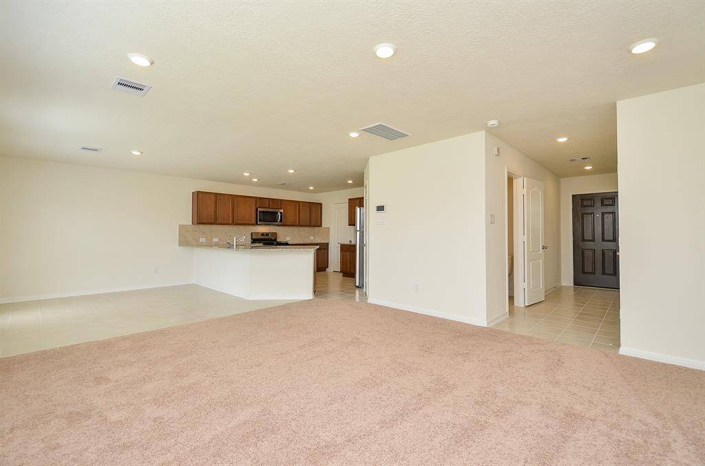 This spacious open-concept living area features a cozy carpeted section, a sleek kitchen with modern appliances, and ample natural light. Ideal for entertaining, it seamlessly connects to other spaces, offering a welcoming and versatile layout.