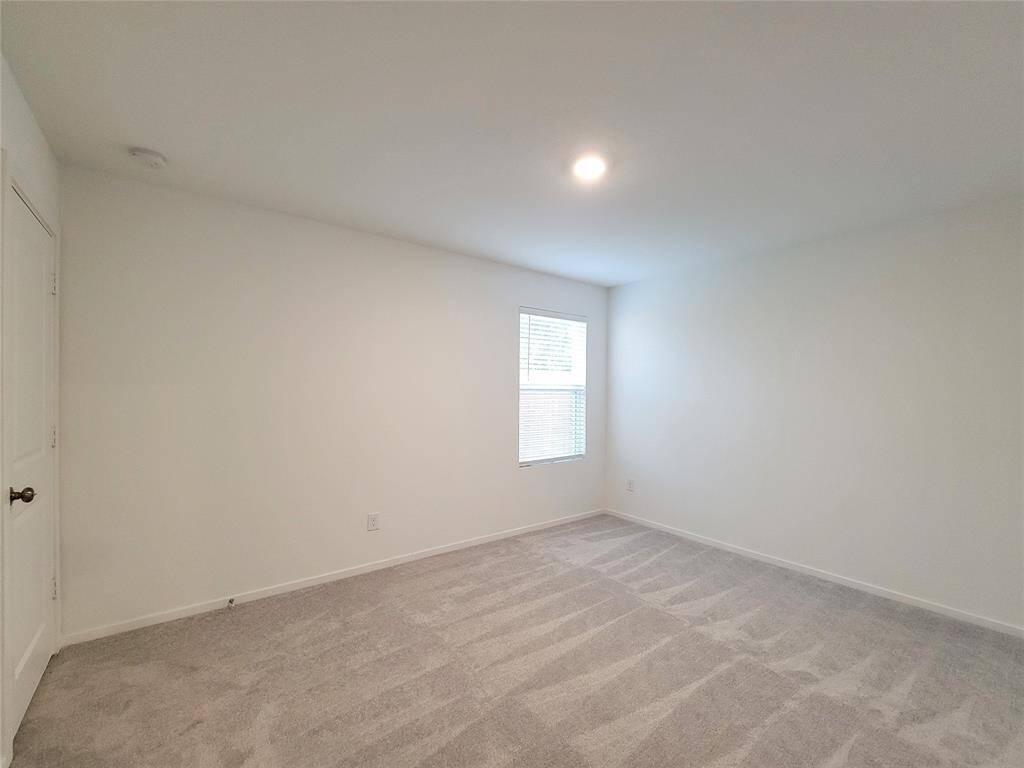 This is a clean, empty room with neutral walls, carpeted flooring, and a single window providing natural light.
