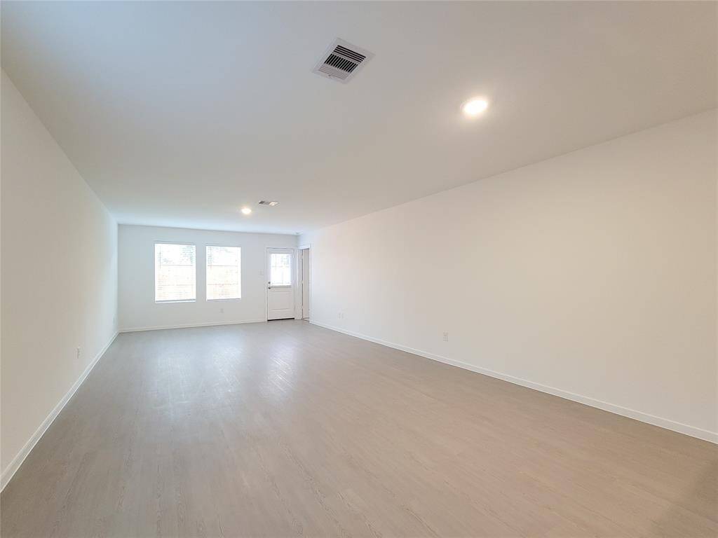 The living room is spacious with modern, new flooring, neutral walls, and ample natural light from two windows. It’s a blank canvas ready for personalization.