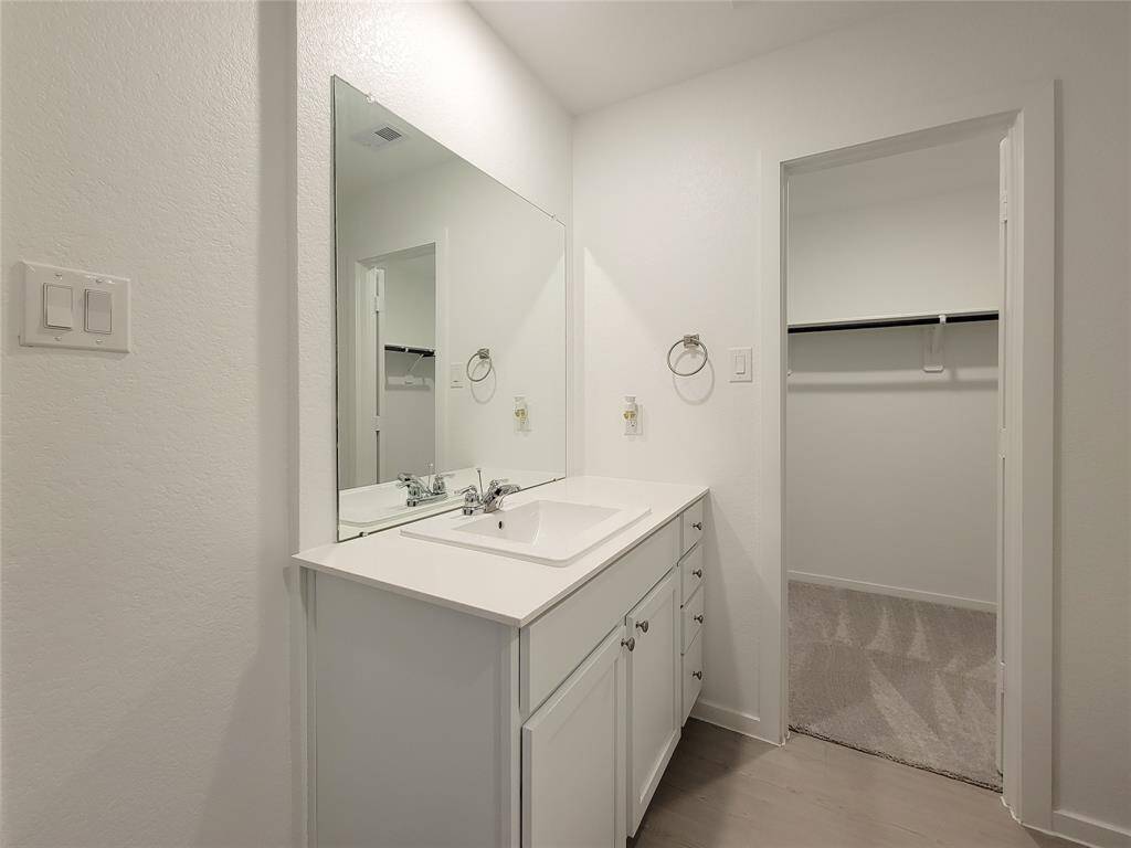 This is a clean, modern bathroom featuring a large mirror, a white vanity with under-sink storage, and bright lighting. There's also a convenient closet for additional storage.