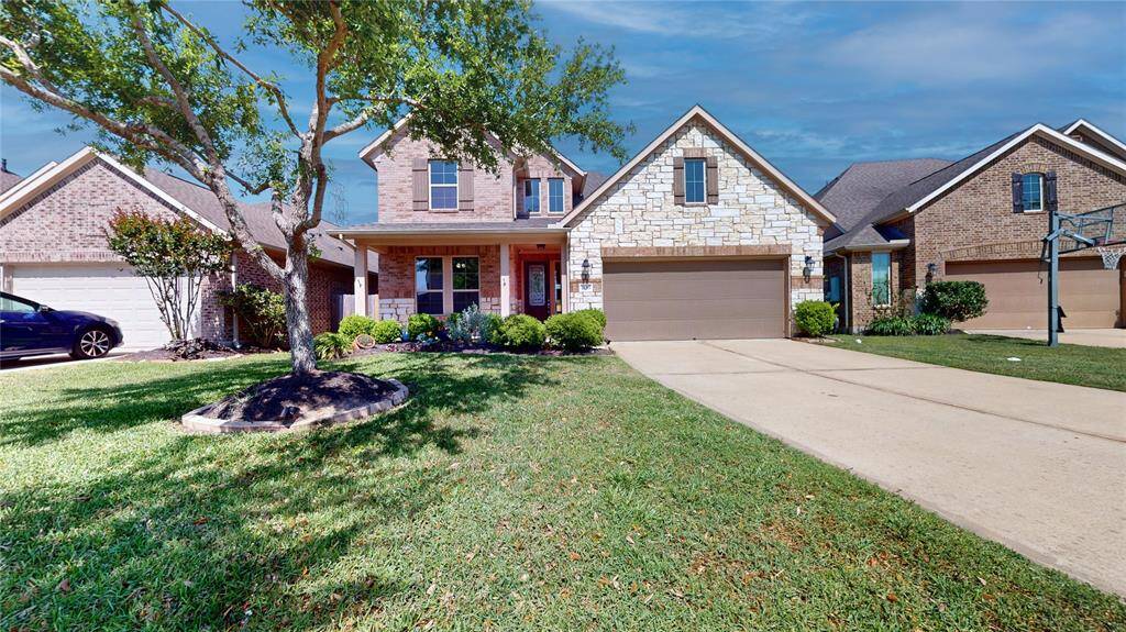 Charming two-story brick and stone home with a well-maintained front yard, two-car garage, and a welcoming porch.